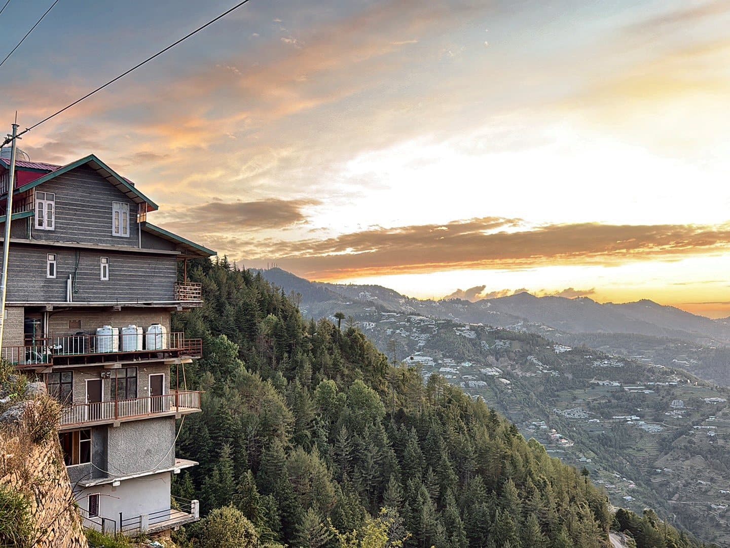 The Pinewood Homestay Kufri, a multi-storey hill house on a forested slope, at sunset