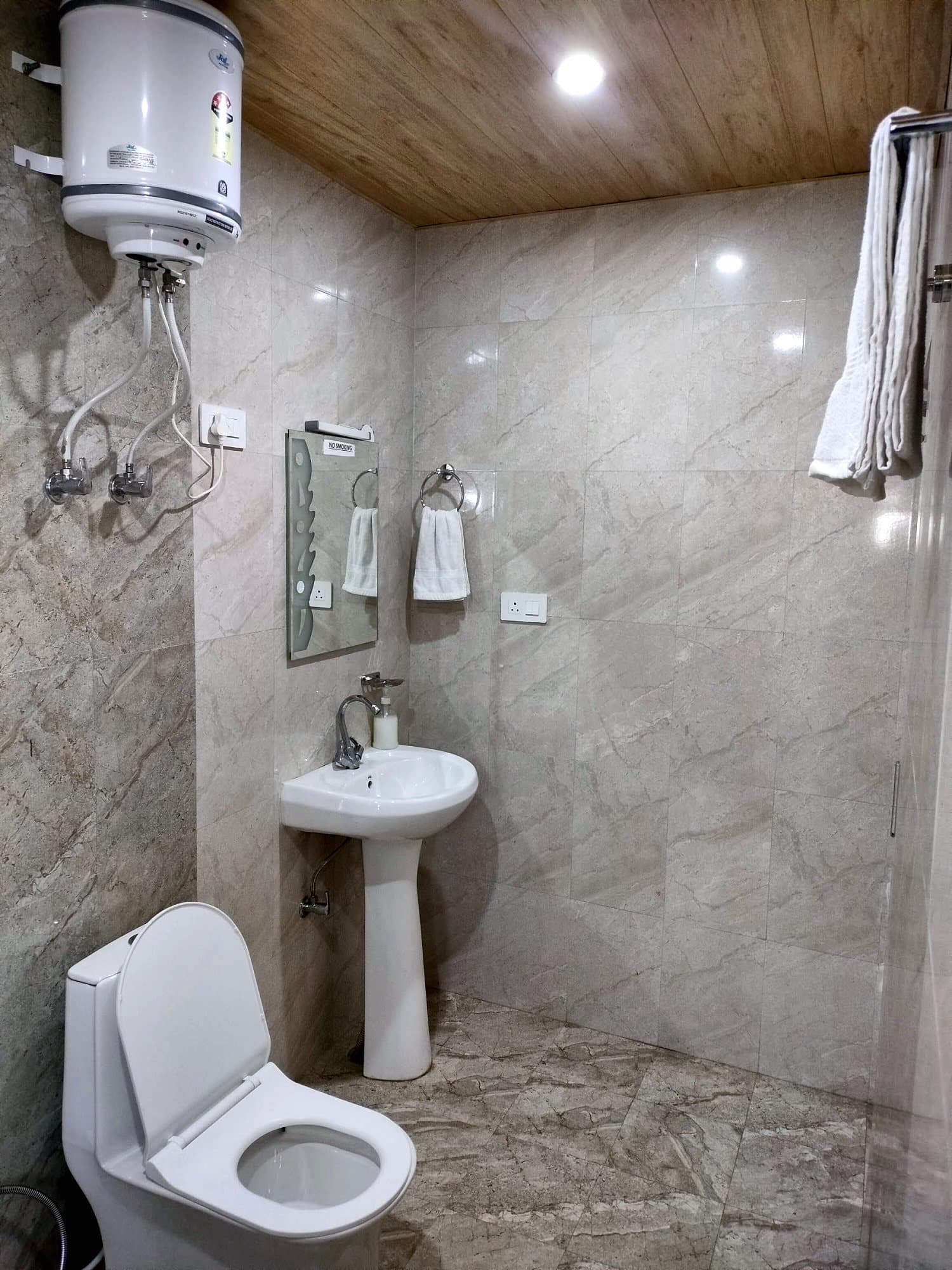 Tiled washroom at Pinewood with washbasin, towel rail and geyser