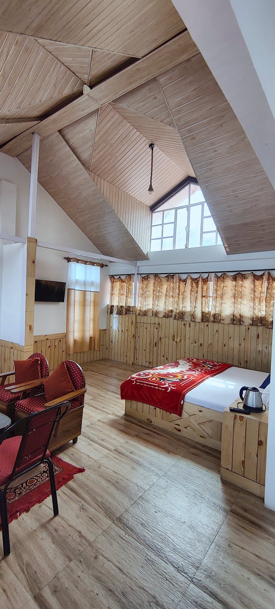 Attic room at Pinewood with a sloped wooden ceiling, double bed, sofa chairs and wooden floor
